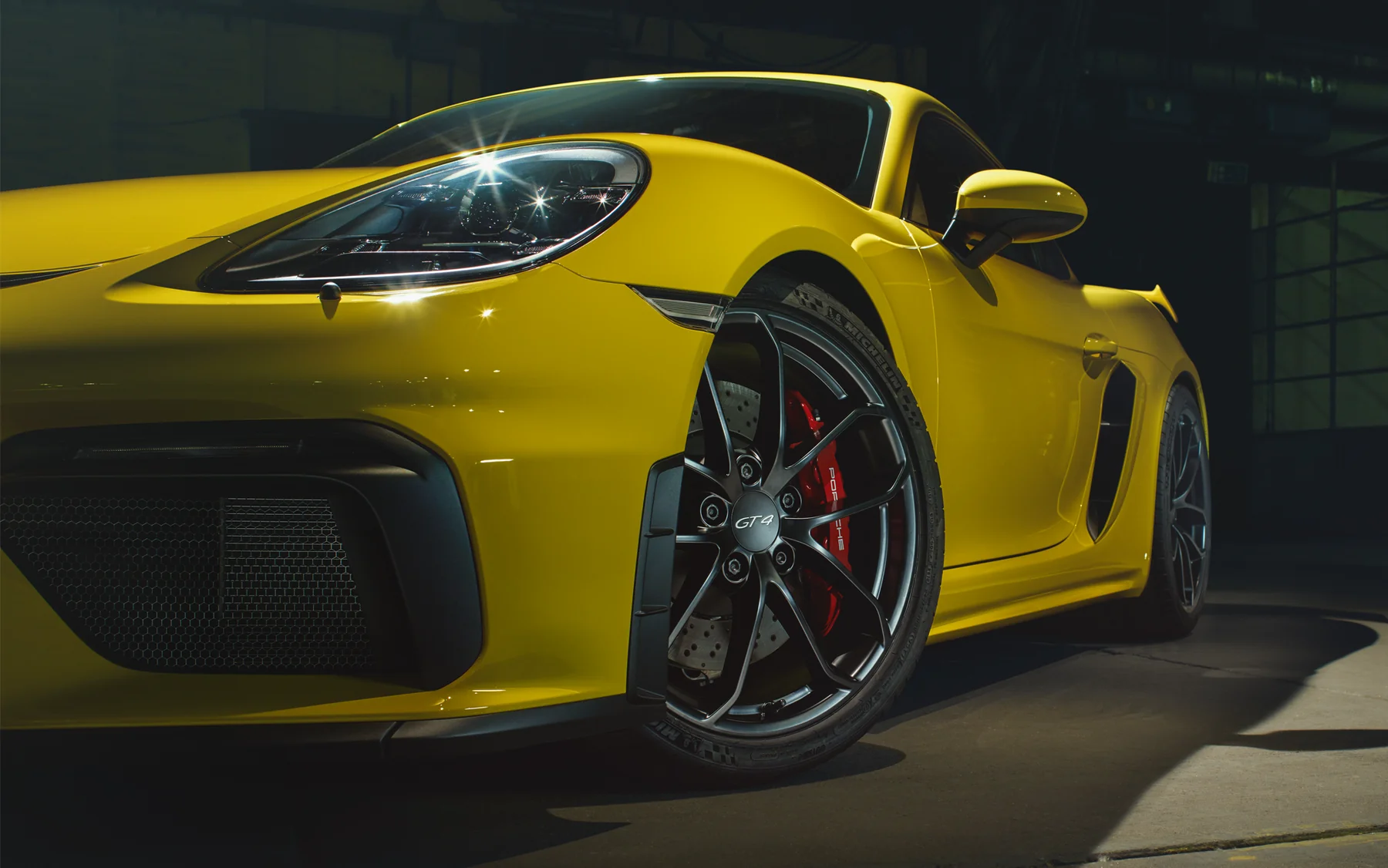 Porsche 718 Cayman GT4 สีเหลือง พร้อมล้อสีดำในบรรยากาศโรงรถ